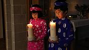 Zwei Kinder in traditionellem vietnamesischen Gewand tragen eine Kerze zum Altar. Sie schauen bedächtig. 